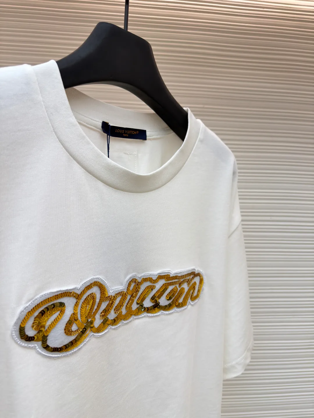LOUIS VUITTON cotton round neck embroidered Vuitton signature logo short sleeves ●Original version: purchased and developed for 12300 ●Item number: 1682272-A10 ●Fabric: cotton fabric ●Technology: embroidery production ●Color: white ●Version: fitted version ●Weight: about 270 grams ●Size: S-M-L-XL ●Description: This white short-sleeved T-shirt is made of high-count combed cotton fabric and has been treated with pre-washing technology. It has a soft and skin-friendly touch and is not easy to deform. The silhouette of the shirt is a loose shoulder design, which meets the needs of modern casual wear. The core decoration area on the chest uses hand-beading and bronzing technology, and uses metallic gold sequins and embroidery threads intertwined to outline a three-dimensional letter pattern. The sequins are layered and inlaid, and each one is manually positioned and fixed by craftsmen to ensure a regular texture and uniform gloss. The edges of the letters are sewn with matte silk thread to form a visual contrast between gold and matte, while reinforcing the decorative structure to avoid falling off during wear. The neckline uses double-needle hemming technology and is matched with ribbed cuffs of the same fabric. It is durable and fits the neck. The overall craftsmanship combines handicraftsmanship with modern clothing technology, and the details show exquisite texture. The overall wiring is straight and delicate, the fabric is comfortable and soft, and the color is consistent without color difference. It can be matched with the same style to create a fashionable look and control various occasions. Customized accessories, complete with three standards, same style for men and women!